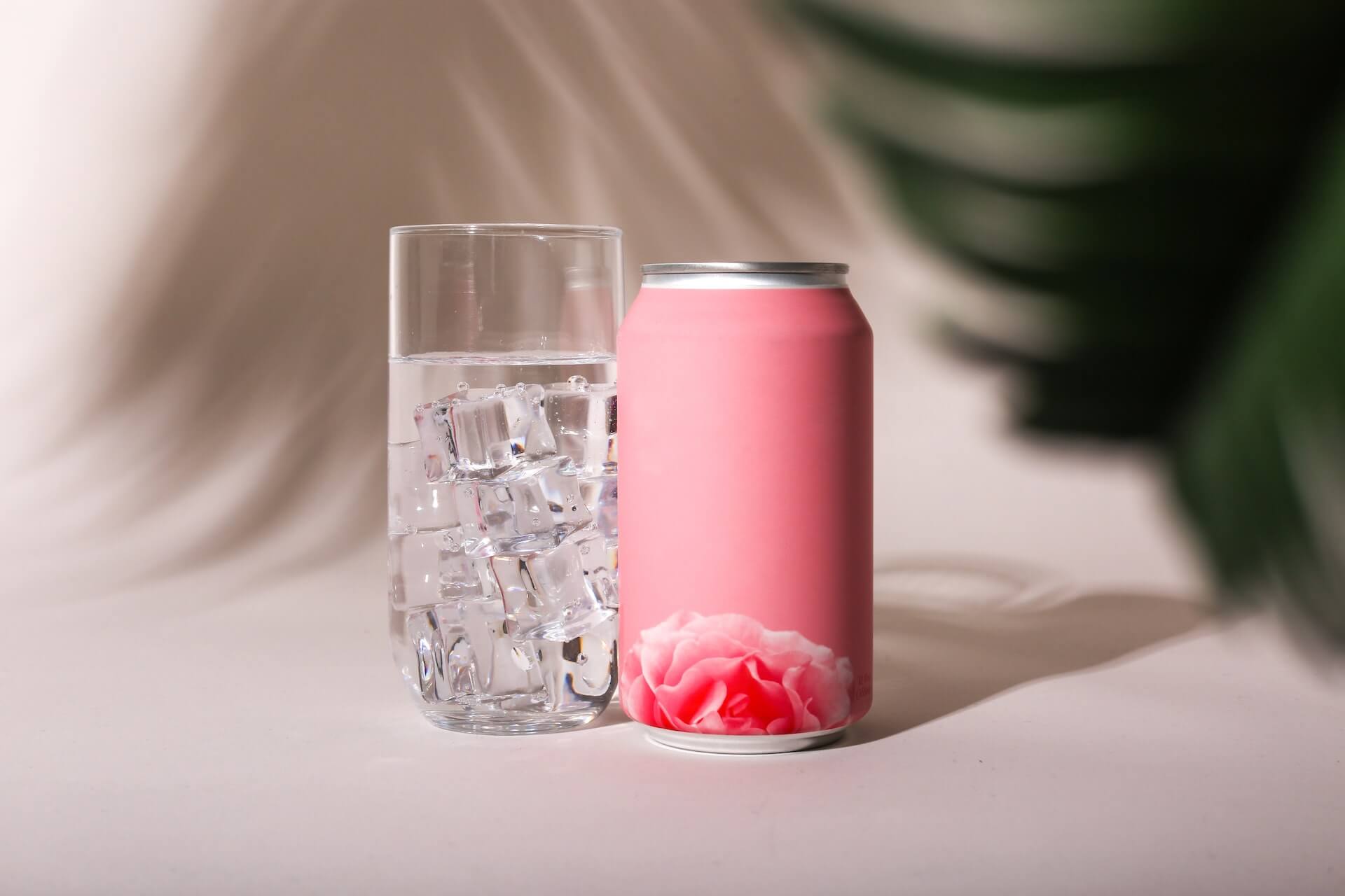 A pink soda can next to a glass of water