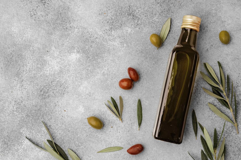 A bottle of olive oil surrounded by fresh olives and green leaves