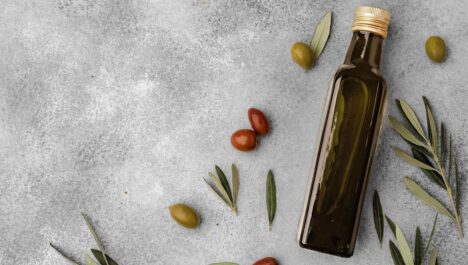 A bottle of olive oil surrounded by fresh olives and green leaves