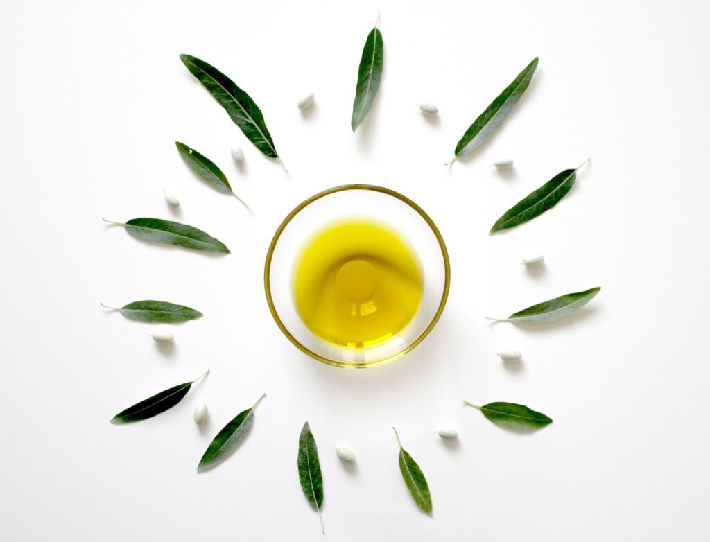 Olive oil in a glass bowl on a white table surrounded by green leaves